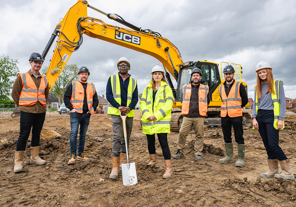 7 people in a row wearing PPE boots, high vis and hats. One leaning on a spade.