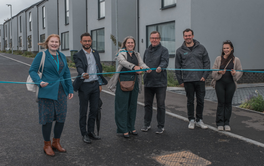 6 people in a street holding a blue ribbon, about to cut it