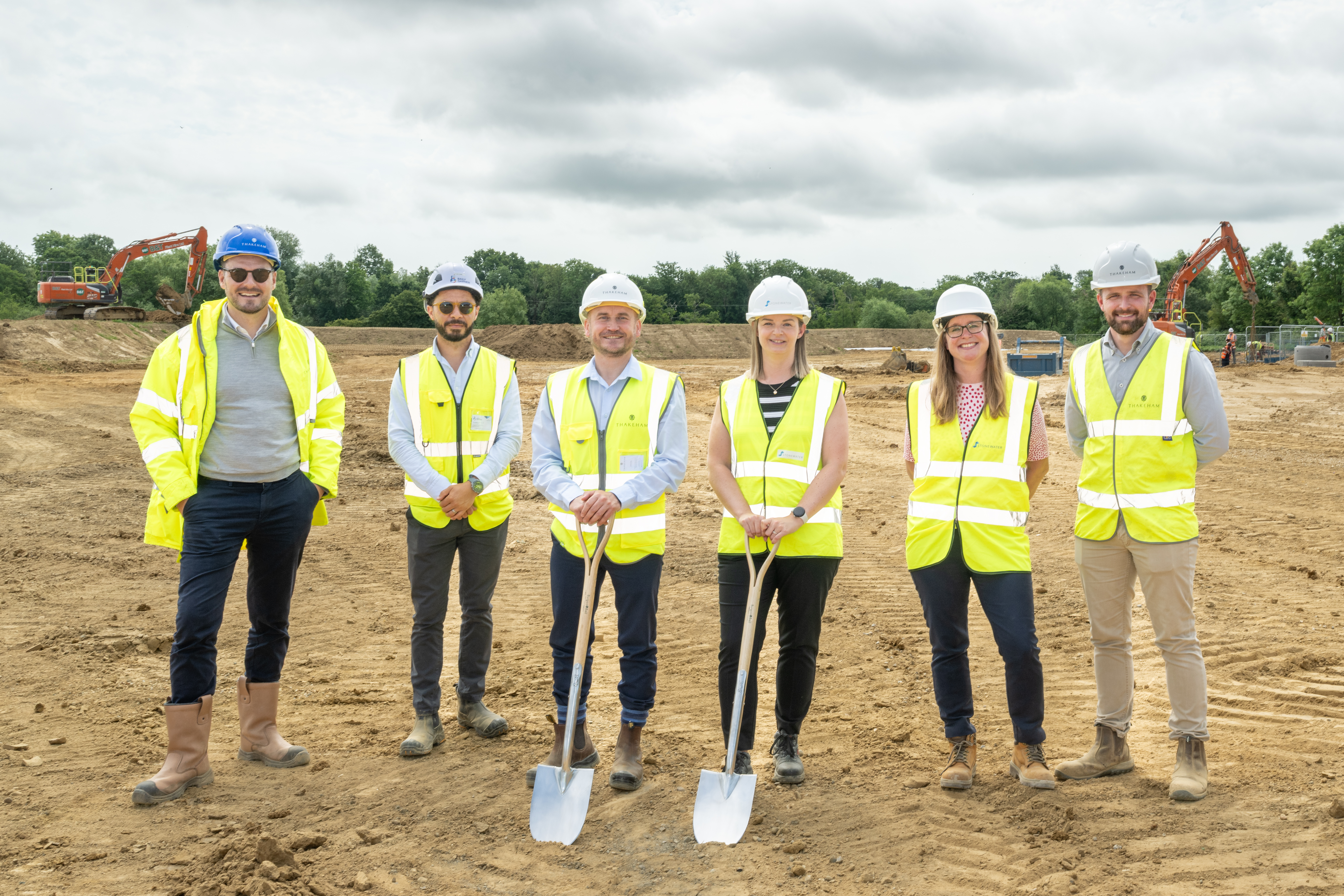 6 people wear PPE on a building site. Two hold spades as a ceremonial spade in the ground.