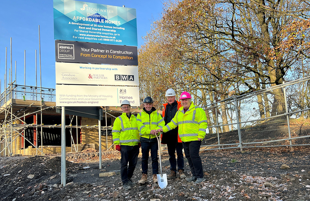 Four people stood smiling, one holding a spade.