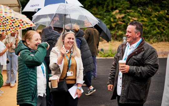 Three colleagues laughing together, the middle one holding an umbrella