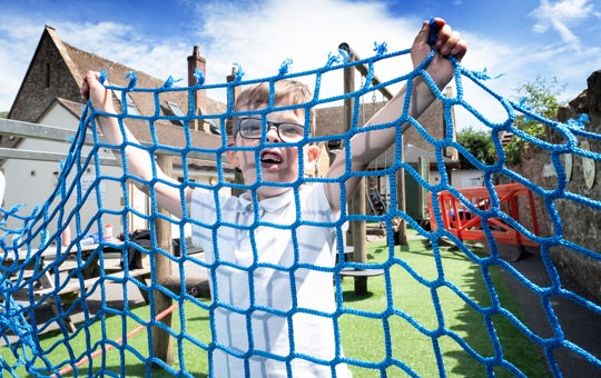 A boy playing behind a net on a playpark