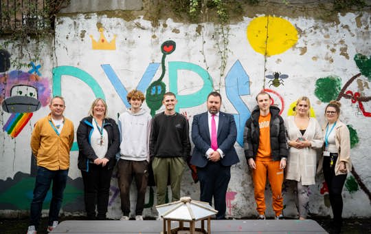 8 people stood in front of graffitied wall