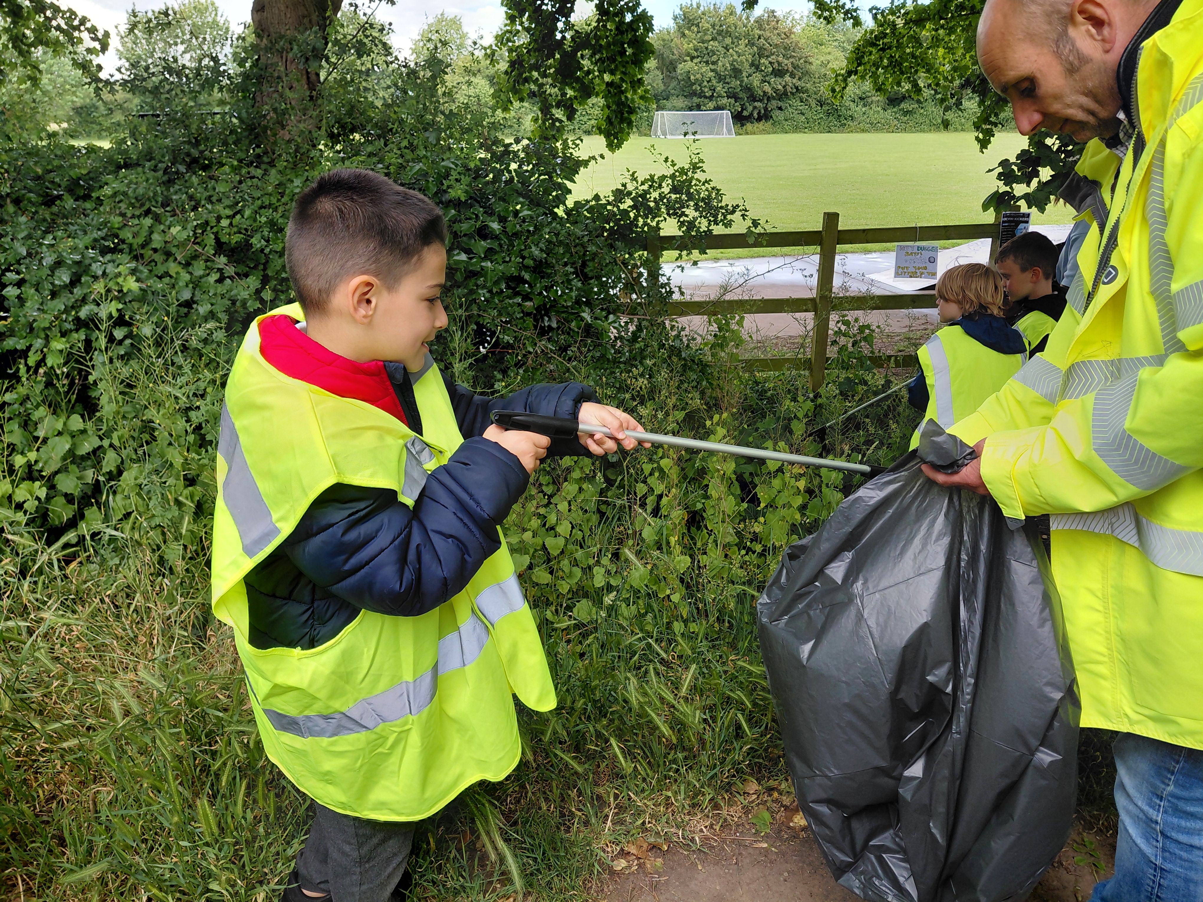 A Hathern Primary School student wearing hi-vis jacket, putting litter into a black bag
