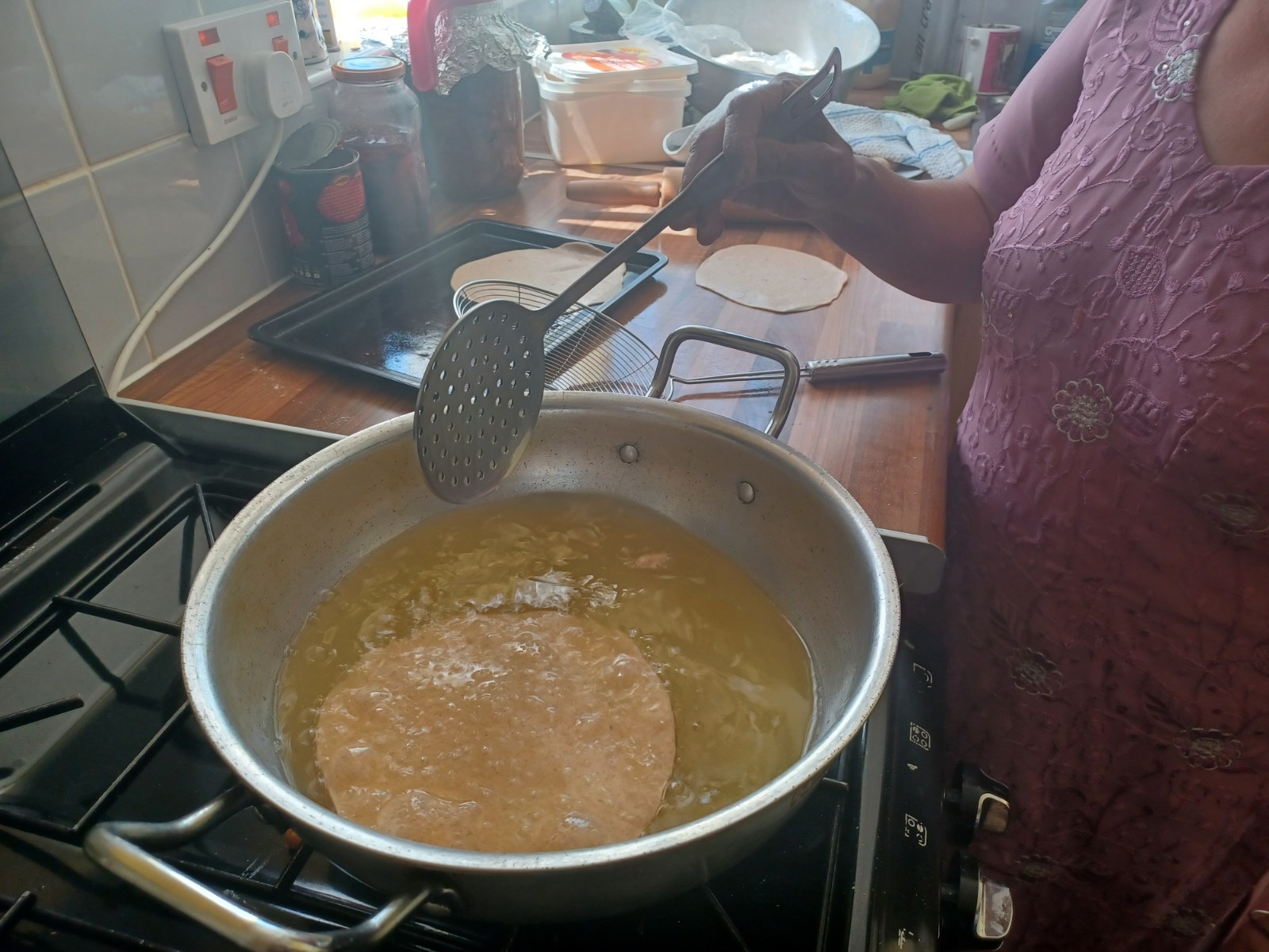 Pan in which a puri, deep fried flatbread, is cooking; a lady stands by with a spatula