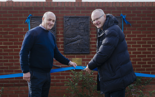 Two men holding a blue ribbon at a ribbon cutting ceremony