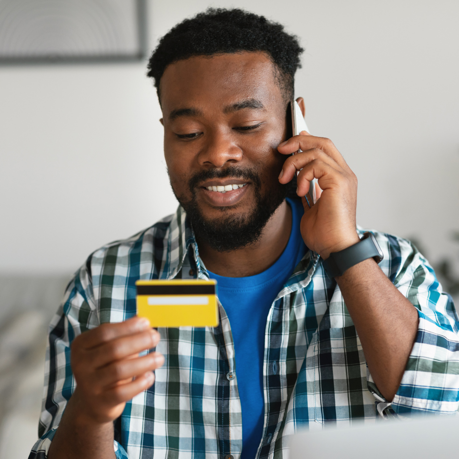Man with phone to his ear in one hand, looking at the credit card he is holding in the other hand